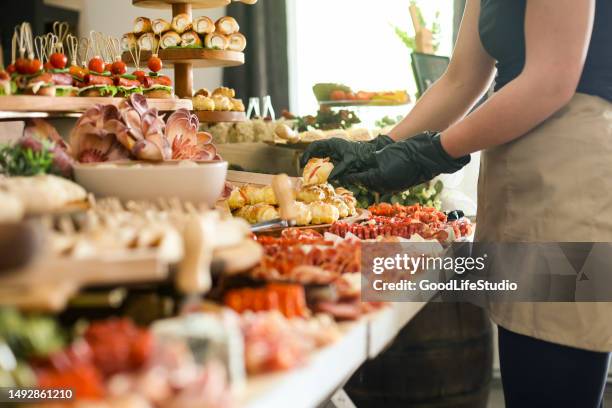 Caterer serving a large buffet table full of delicious food. Unrecognizable Caucasian female.
